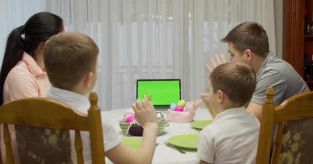 Notebook met groen scherm. Ouders met twee tienerjongens praten videogesprek met een laptop, genieten van tijd samen doorbrengen in het weekend, thuis, aan de vakantietafel voorbereid op Pasen — Stockvideo