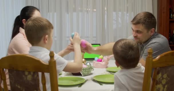 Eine vierköpfige Familie plaudert, isst und sitzt am Tisch. Auf dem Tisch liegt ein Computer mit grünem Bildschirm — Stockvideo