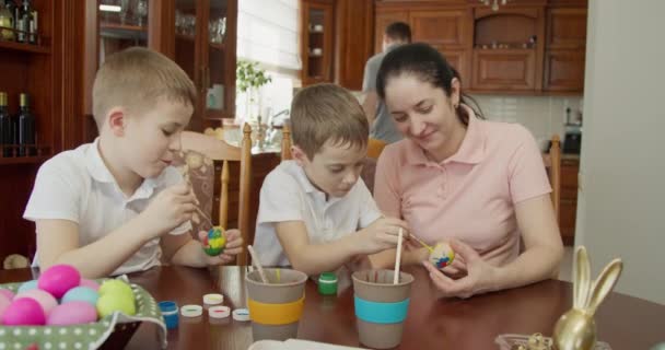 Mama hilft ihren Söhnen beim Bemalen von Ostereiern. Osterstimmung — Stockvideo