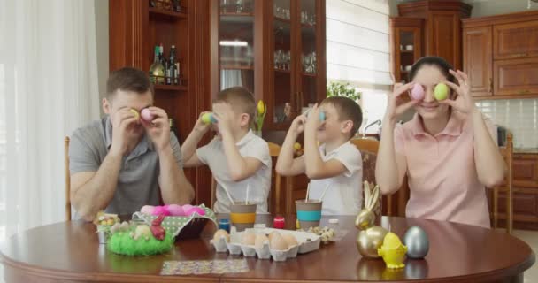 Familia alegre que se divierte preparándose para la Pascua y poniendo huevos de colores a los ojos — Vídeos de Stock