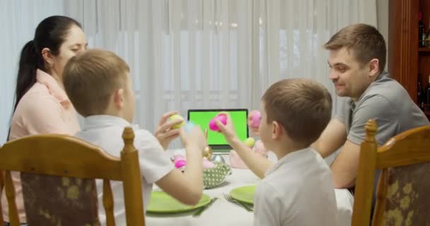 Grön skärm anteckningsbok. Föräldrar med två tonårspojkar pratar videosamtal med en bärbar dator, njuter av att tillbringa tid tillsammans på helgen, hemma, vid semesterbordet förberedd för påsk — Stockvideo