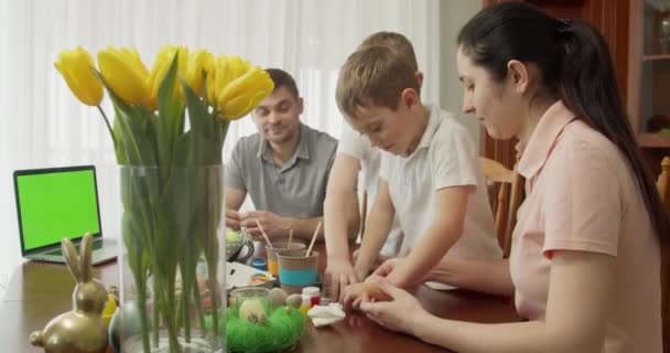 Familjen sätter klistermärken på äggen. på bordet finns en dator med grön skärm — Stockvideo