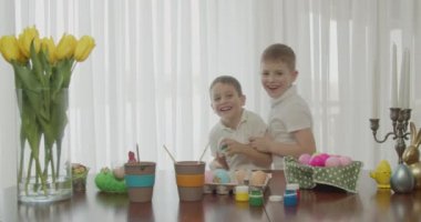 İki küçük kardeş gülümsüyor, birbirlerini gıdıklıyor ve paskalya yumurtası boyuyorlar.