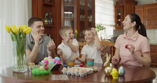 Vierköpfige Familie lächelt, bemalt Eier und zeigt, in welchen Farben sie Eier bemalt hat — Stockvideo