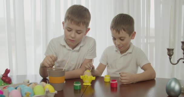 Deux frères vêtus de T-shirts blancs peignent un oeuf de poulet sur un porte-oeuf jaune — Video