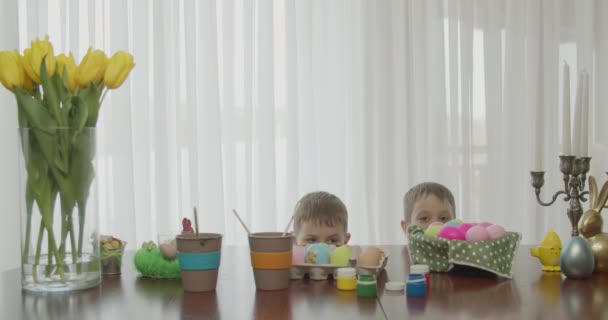 Dois irmãos saltam como coelhos. na mesa estão ovos coloridos e ferramentas para pintar ovos — Vídeo de Stock