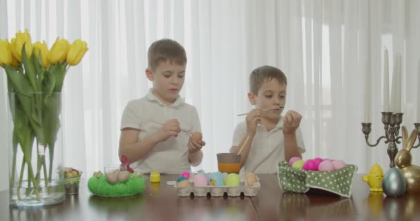 Ambiente pascal. dois irmãos desenhar ovos com uma escova. — Vídeo de Stock