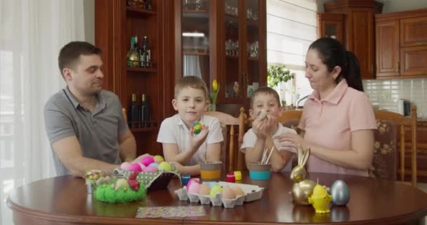 Familia divirtiéndose mientras pinta y decora huevos para las vacaciones — Vídeo de stock