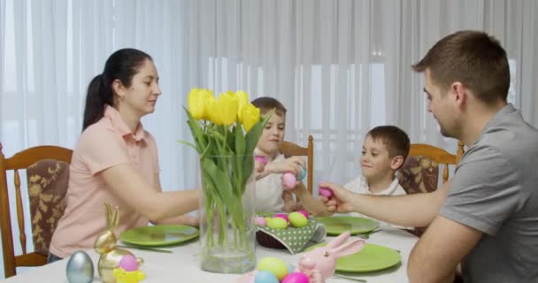 Család ül az ünnepi asztalnál, összecsapnak színes tojások. húsvéti vacsora — Stock videók