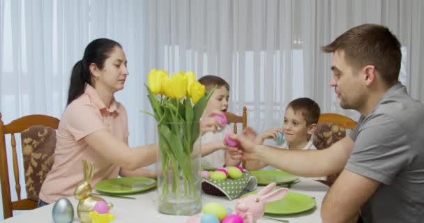 Сім'я сидить за святковим столом, зіштовхується з різнокольоровими яйцями. Великодня вечеря — стокове відео