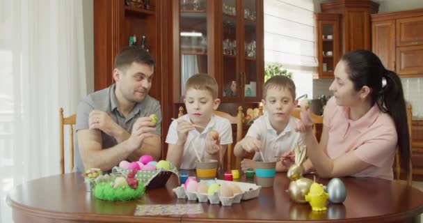 Ευτυχισμένη οικογένεια ζωγραφίζει πασχαλινά αυγά στην κουζίνα — Αρχείο Βίντεο