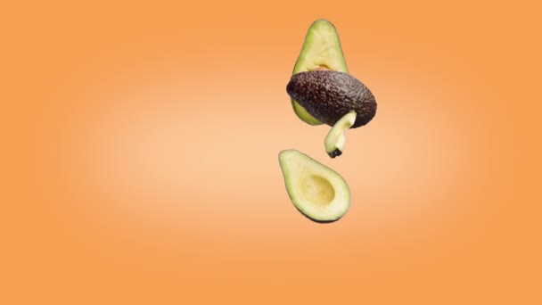 Avocado halves and slices that fall on the Orange background. — Stock Video