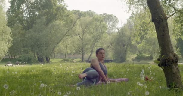 A young brunette in a sports uniform in a supine position exercises her legs with an elastic expander to pump her leg muscles in an outdoor park. — Stok video