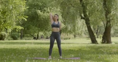 Güzel atletik vücudu ve örülmüş kasları olan, sabah antrenmanından önce parkta ısınırken kollarını kaldıran bir kadın. Genç sporcu dışarıda egzersiz yapıyor.