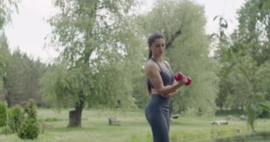 Yetişkin bir kadın omuz kaslarını çalıştırıyor ve bir dambılı kaldırırken dirseğini esnetiyor.