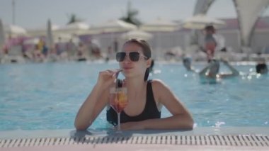 Güneş gözlüklü bayan havuzda kokteyl içer. Havuz kenarında yaz tatilinin tadını çıkaran kadın..