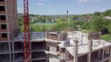 İnşaat halindeki bir evin çatısındaki bir grup inşaat işçisinin hava manzarası ve bir kule vinci.