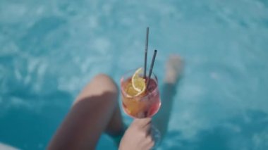 cocktail in the hands of a woman by the pool. The feet float in the pool water. Selective focus. basin.