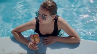 Güneş gözlüklü bayan havuzda kokteyl ile oturuyor. Havuz kenarında yaz tatilinin tadını çıkaran kadın..