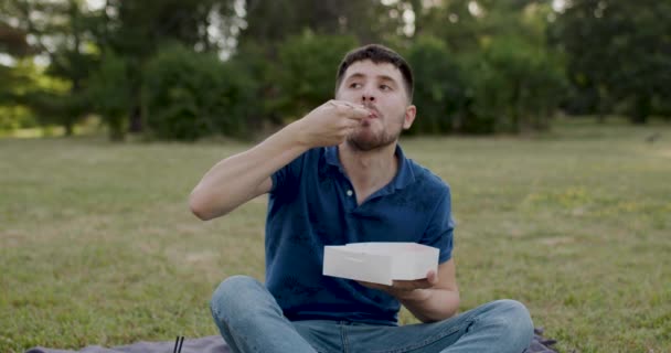 Man Blue Shirt Sitting Grass Woods Puts Sushi His Mouth — Stockvideo