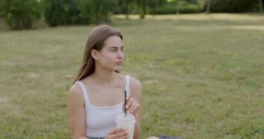young brunette dressed in white, drinks a white lemonade and looks straight ahead 