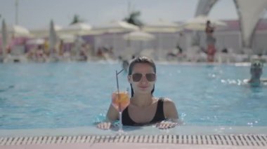 Woman is in the pool, next to the pool is a cocktail