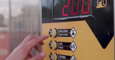 View of the coin machine with a mans hand selecting a button to wash the car with a water gun at the manual self-service car wash. automated car wash with self-service