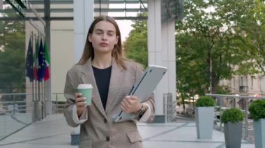 portrait of a focused business woman going to the meeting at the office. serious business woman, in a suit, with a computer in her hand, and a coffee, in the background of a business center