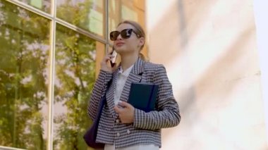 the cheerful student walks by the university and talks on the phone. concept of a busy student who combines both college and a job.