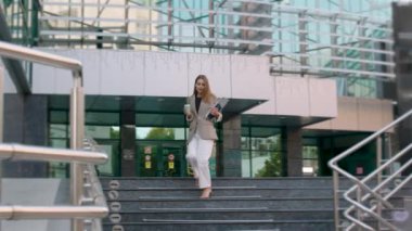 business woman, dressed in a suit and high heels, very elegantly descends the stairs of a business center. Brunette woman with coffee and computer in hand.