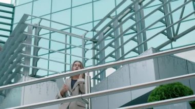 a business woman came out of the office and while talking on the phone approached a railing. elegant woman, holding a computer. Very large and modern style office.