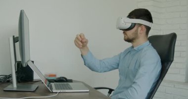 A handsome man in a shirt wearing virtual reality glasses. Man touches something with hands using modern 3D glasses indoors.