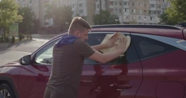 side view where a worker from the car wash wipes the car in the last stage of cleaning. open type car wash. Burgundy luxury car