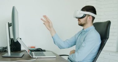 Üç boyutlu gözlük takan ciddi bir adam, düşünceli bir şekilde oturuyor ve analiz ediyor. Koyu renk saçlı adam, klasik giyinmiş, işinde ona yardımcı olan modern teknolojilere sahip.. 