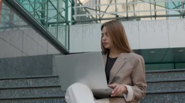 Uzun ve modern bir ofisin merdivenlerinde oturan esmer kadın bilgisayarda çalışıyor ve telefonlara cevap veriyor. Çok meşgul bir kadın girişimci kavramı.