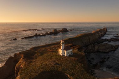 Oregon sahilindeki Cape Arago Deniz Feneri. Batan güneş binayı aydınlatıyor.. 