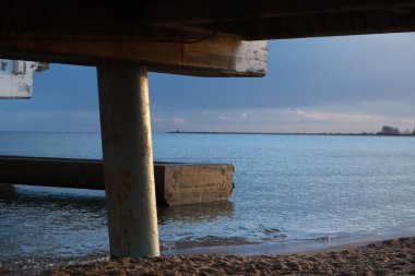 İskelenin altındaki deniz suyunun manzarası. İskelenin kolonları. Denizde iskele. Dalgalar denizin sularında. İskeleye yakın çekim.