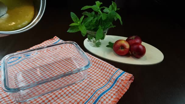 Ricetta strudel di mele. l'impasto viene versato in una teglia su fondo nero. sul tavolo accanto a un bicchiere di menta e 3 mele mature — Video Stock
