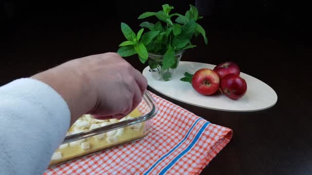 Przepis strudel jabłko. jabłka są wlewane przez kucharza do naczynia do pieczenia na czarnym tle. na stole obok szklanki mięty i dojrzałych jabłek — Wideo stockowe