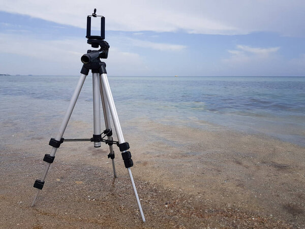 a tripod for the phone and the phone is installed on a sandy beach. a blogger shoots a story for a blog on vacation