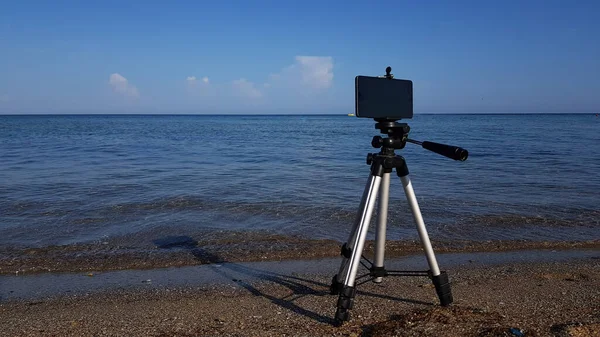 電話用の三脚と電話が砂浜に設置されています ブロガーが休暇中にブログの記事を撮影し — ストック写真