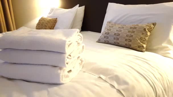 Kar beyazı havlular beyaz çarşaflar tarafından karıştırılan yatağın üzerinde düzgünce katlanır. Otel odası. — Stok video
