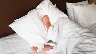 a person lies in bed and covers his head with a pillow