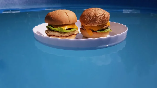 白いトレイの上に2ジューシーな美しいハンバーガーは青い水で泳ぐ 高級ホテルでは食事はプールで提供され — ストック写真