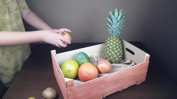 Fruitverpakking houten geschenkdoos. een man pakt een geschenk van ananas mango kiwi op een donkere achtergrond — Stockvideo