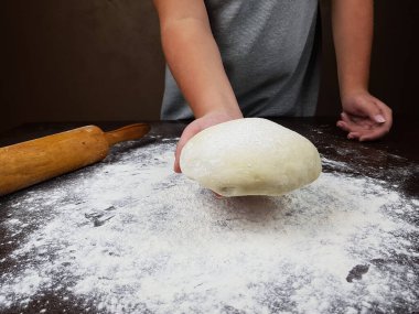 Aşçı elinde mantar hamuru tutuyor. Masada hamuru yuvarlamak için bir merdane var. Masaya un serpilmiş.