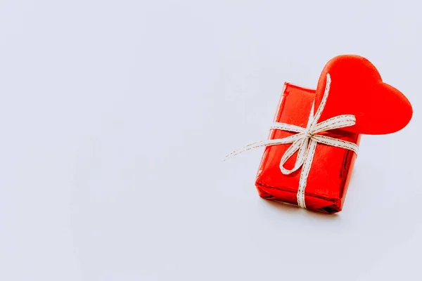The concept of Valentines Day. A red stuffed toy heart and a red gift box with a white ribbon on a light background. Banner. Copy the space of your text. Greeting card