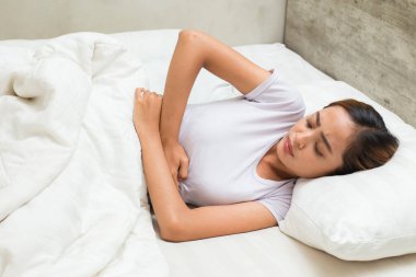 Genç Asyalı kadın uyuyor ve midesi ağrıyor. 