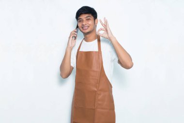 Mutlu Asyalı genç barmen ya da garson kız beyaz arka planda izole edilmiş cep telefonu kullanıyor.