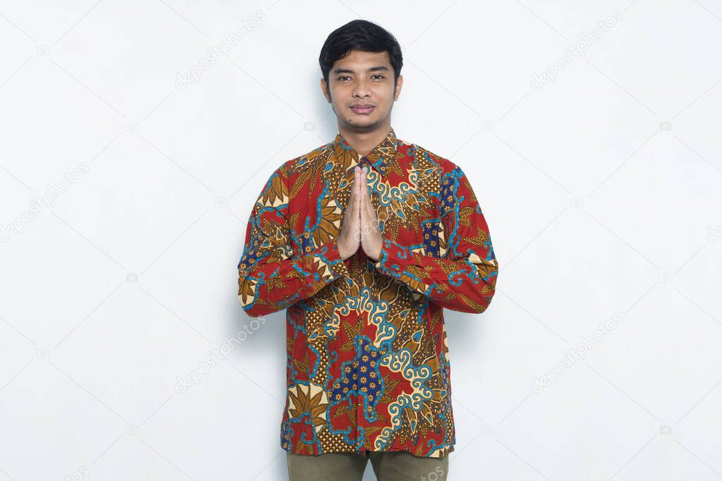 portrait of young javanese man wearing batik showing welcome hand gesture isolated on white background